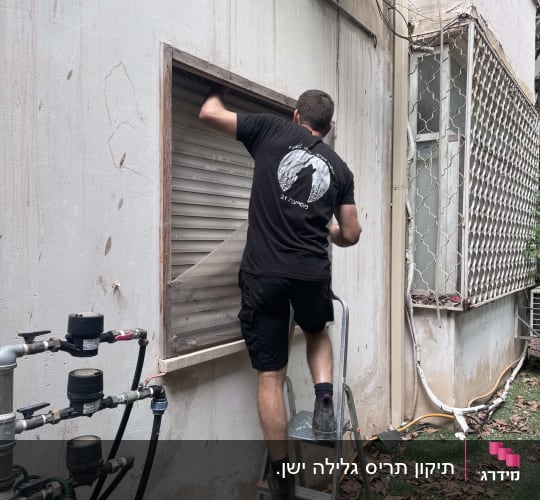 אדם מתקן תריס גלילה על סולם ליד קיר חיצוני